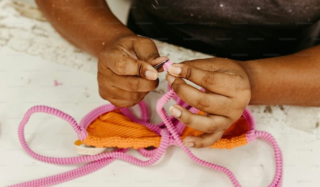 Mains de femme en train de coudre un soutient-gorge rose et orange