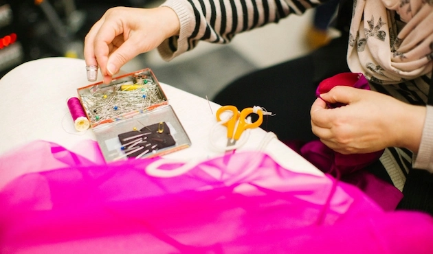 Mains de femme en train de manipuler une boîte à épingles et du tissu rose