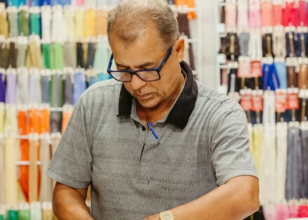 Homme en train de travailler dos à un mur de fils de couture des toutes les couleurs